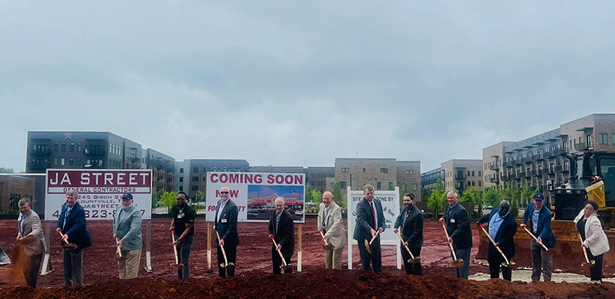 Photo of a line of people shoveling dirt at a ground breaking ceremony.